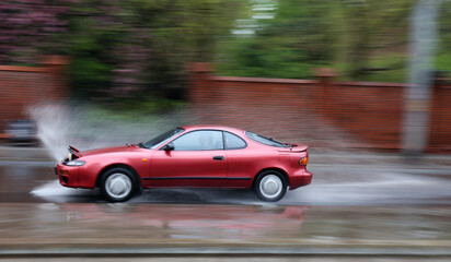 Samochód wpada w kałużę wody na jezdni powodująć rozbryzg.  - obrazy, fototapety, plakaty