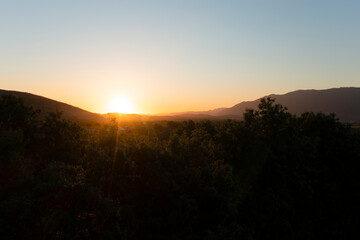 View from above, stunning aerial view of a valley illuminated by a beautiful sunset in the distance. Rural landscape surrounded by a mountain range, Italy.