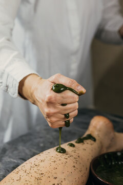 Seaweed massage. Body treatment with seaweed to reduce cellulite and skin aging. Close-up of hand applying clay on leg.