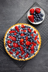 Delicious blueberry and strawberry tart with whipped cream and mascarpone on a dark stone background. Top view.