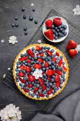 Delicious blueberry and strawberry tart with whipped cream and mascarpone on a dark stone background. Top view.