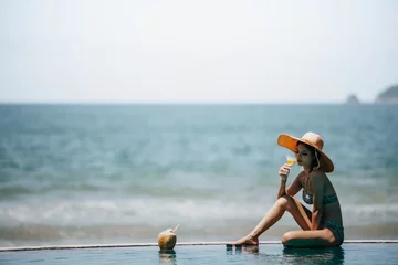 Fotobehang Beautiful Young Woman Wearing Hat Sitting By Swimming Pool Against Sea © ic36006