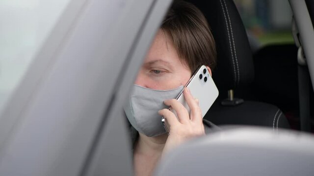 Woman with protective face mask talking on mobile phone from her car while driving during pandemics