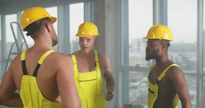 Shirtless diverse builders at construction site talking