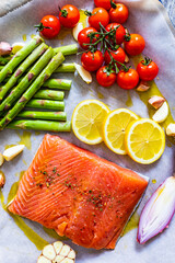 Fresh raw salmon steak with asparagus, cherry tomatoes, lemon, garlic and onion on cooking pan prepared to roast