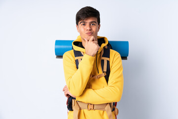 Young mountaineer man with a big backpack over isolated blue background laughing