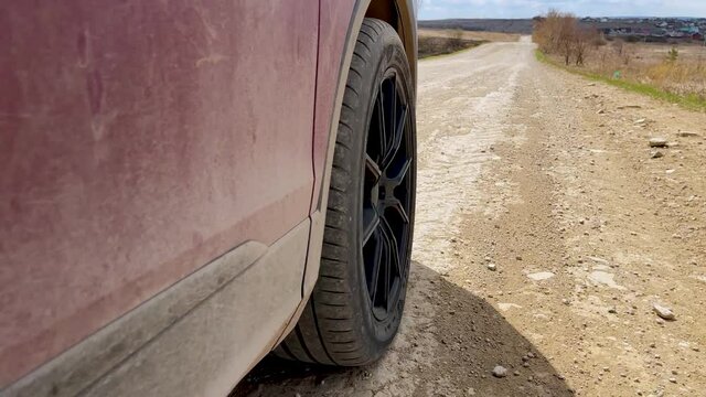 Video recording in motion, red and maroon car dirty and dusty, driving on a dirt road at speed, side view . The wheel with the black disc turns. The camera repeats the terrain of the road.
