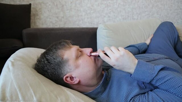 Man removes nose hair with a trimer lie sofa