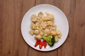 Rice with pieces of chicken meat and vegetables on a plate. On a wooden table, top view