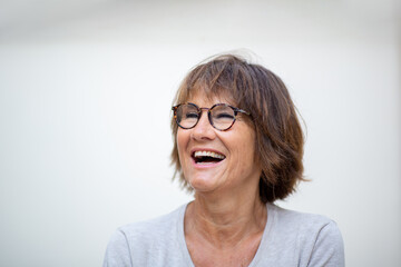 Close up older woman laughing with eyeglasses against white background and looking away