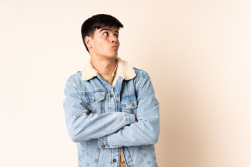 Handsome man over isolated beige background making doubts gesture while lifting the shoulders