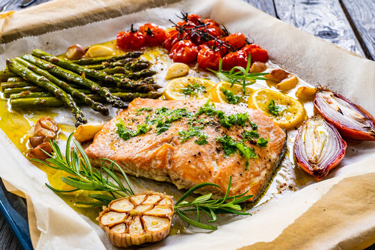 Sheet Pan Dinner - Roasted Salmon Steak With Asparagus, Lemon ,rosemary, Tomatoes, Onion And Garlic On Cooking Pan On Wooden Table
