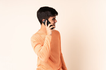 Handsome man over isolated beige background keeping a conversation with the mobile phone with someone