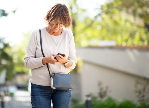 Older Woman Standing Outside Looking At Mobile Phone