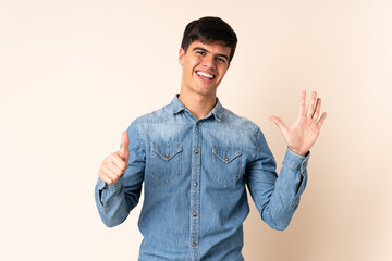 Handsome man over isolated beige background counting six with fingers