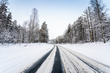Snowfall on a winter day, snow-covered country road. View from the side of the road. Coniferous forest. Russia, Europe. Beautiful nature.