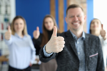 Successful young businessman showing thumb up against background of colleagues closeup