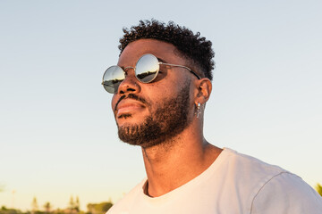 Face portrait of a handsome black and young american man wearing sunglasses and smiling during sunset at the beach