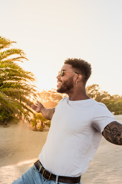 Portrait of a handsome black and young american man wearing sunglasses and smiling during sunset at the beach