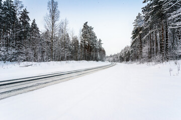 Snowfall on a winter day, snow-covered country road. View from the side of the road. Coniferous forest. Russia, Europe. Beautiful nature.