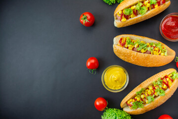 Hot dog with pickles, tomatoes and lettuce on a dark background. Fast food. Calorie food. View from above. Space for copy.