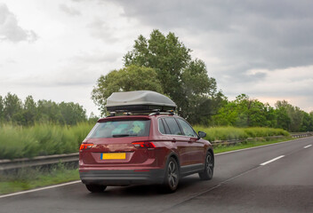 Red car with gray roof luggage box driving on road