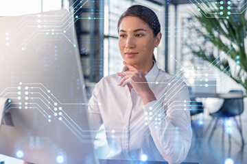 Attractive businesswoman in white shirt at workplace working with laptop to optimize development by implying new technologies in business process. Hi tech hologram over office background