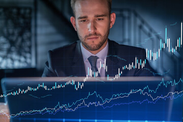 Handsome businessman in suit at workplace working with laptop to optimize trading strategy at...