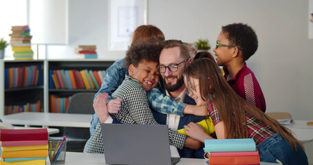 Multiethnic preteen children hugging male teacher in classroom