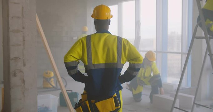 Back view of african foreman in uniform supervising team of builders at construction site