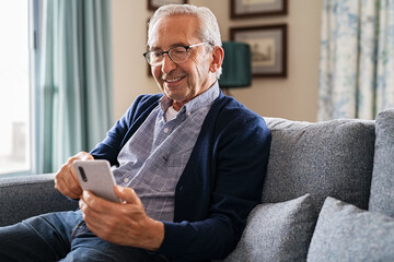 Happy senior man using phone at home - obrazy, fototapety, plakaty