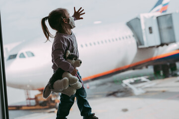 Toddler girl at airport in face mask holding a toy.