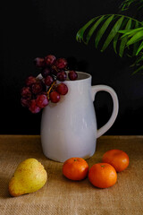 Beautiful, still-life vertical photograph of fruit arranged around a white jug, set against a black background.