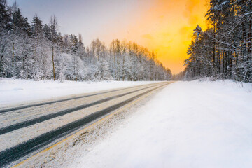 Fototapeta na wymiar Sunrise on a clear winter morning, road passing through the forest in the snow. View from the side of the road. Coniferous forest. Russia, Europe. Beautiful nature.