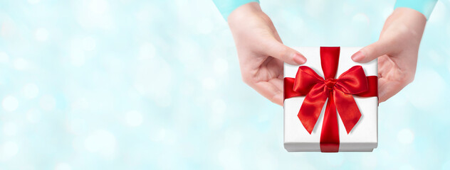 雪の降る中、赤いリボンをかけたプレゼントの箱を渡す女性
