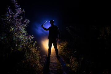 strange light in a dark forest at night. Silhouette of person standing in the dark forest with light. Horror halloween concept. strange silhouette in a dark spooky forest at night