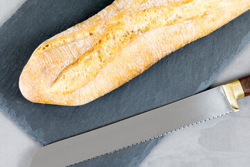 french baguette bread with knife on black cutting board on grey concrete background. Diagonal.