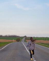 A young girl runs along the road. A girl with long blond hair runs away alone on a deserted road that goes into the distance among the fields. Healthy lifestyle.