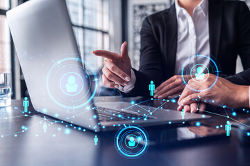 Two HR specialists analyzing the recruitment market using laptop to boost the intern program at international consulting company. Social networking hologram icons.