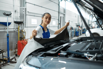 Female mechanic stands at the hood, car service