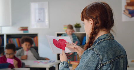 Close up of preteen schoolgirl holding paper with red painted heart standing in classroom