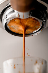 Close-up of coffee being brewed by machine flowing through portafilter into clear glass