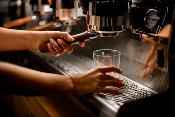 Fototapeta na wymiar Woman barista prepares and pours coffee drink into glass with professional coffee machine