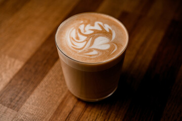 view of glass of hot coffee with beautiful latte art on wooden table background.