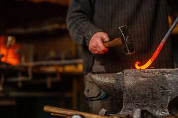 The blacksmith twists the spiral with a sledgehammer, placing a red-hot iron blank on the anvil. Work in the forge