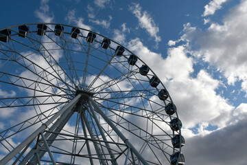 Part of the Ferris wheel with closed booths against a background of blue sky and clouds