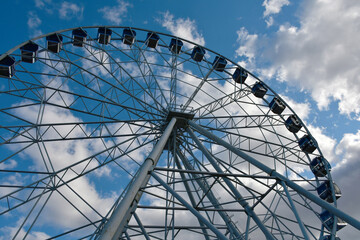 Part of the Ferris wheel with closed booths against a background of blue sky and clouds