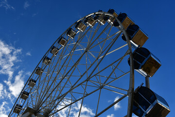 Fototapeta na wymiar Part of the Ferris wheel with closed booths against a background of blue sky and clouds