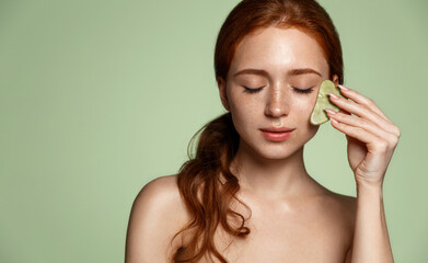 Skin care spa tcm. Redhead woman self massage facial skin with natural jade gouache guasha scraper....