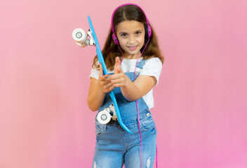 Smiling little girl in headphones with skateboard isolated over pink background